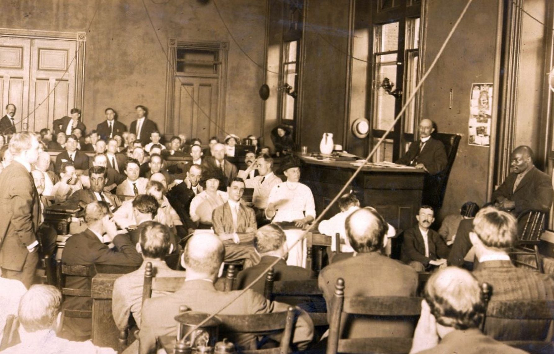 Photo of the trial of Leo Frank, shot on July 28, 1913. Prosecutor Hugh Dorsey, standing at left, is examining witness Newt Lee, at right. Leo Frank who is seated in the centre (Page 3 of Atlanta Journal July 29, 1913)