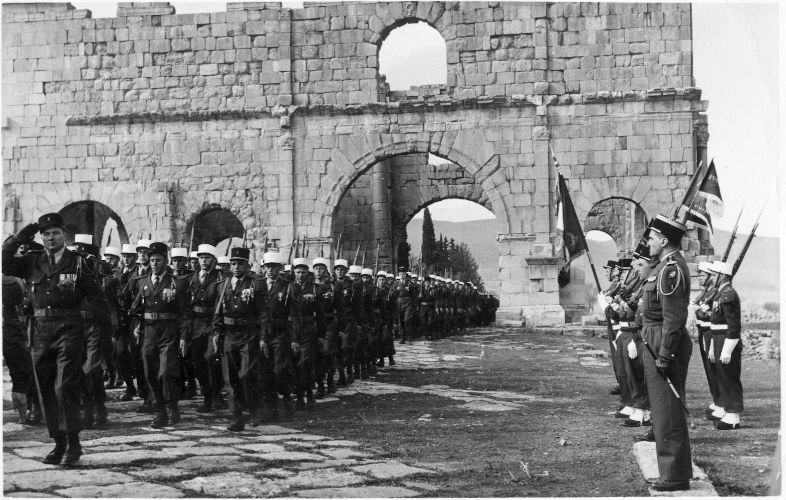 The 13th Demi-Brigade of the Foreign Legion parading through Roman ruins in Lambaesis, Algeria, 1958 (Wikipedia)